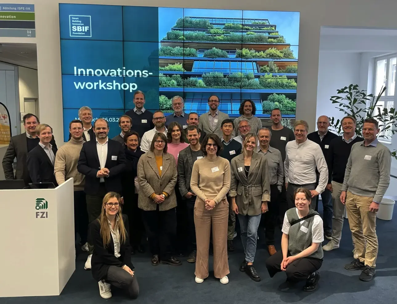 Teilnehmende eines Workshops stehen vor einer Leinwand mit Workshop-Inhalten, im Vordergrund Flipcharts und Material. Die Atmosphäre wirkt konzentriert und offen.